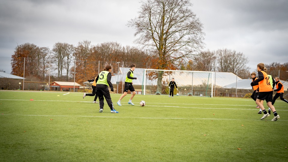 Elever på fotbollsakademin tränar fotboll på gräsplan.
