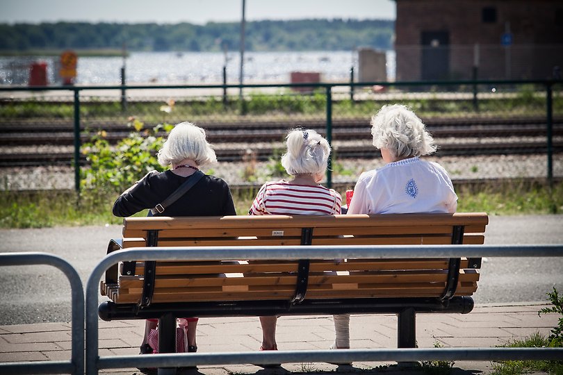 Tre gamla damer sitter på en bänk och väntar på bussen. 